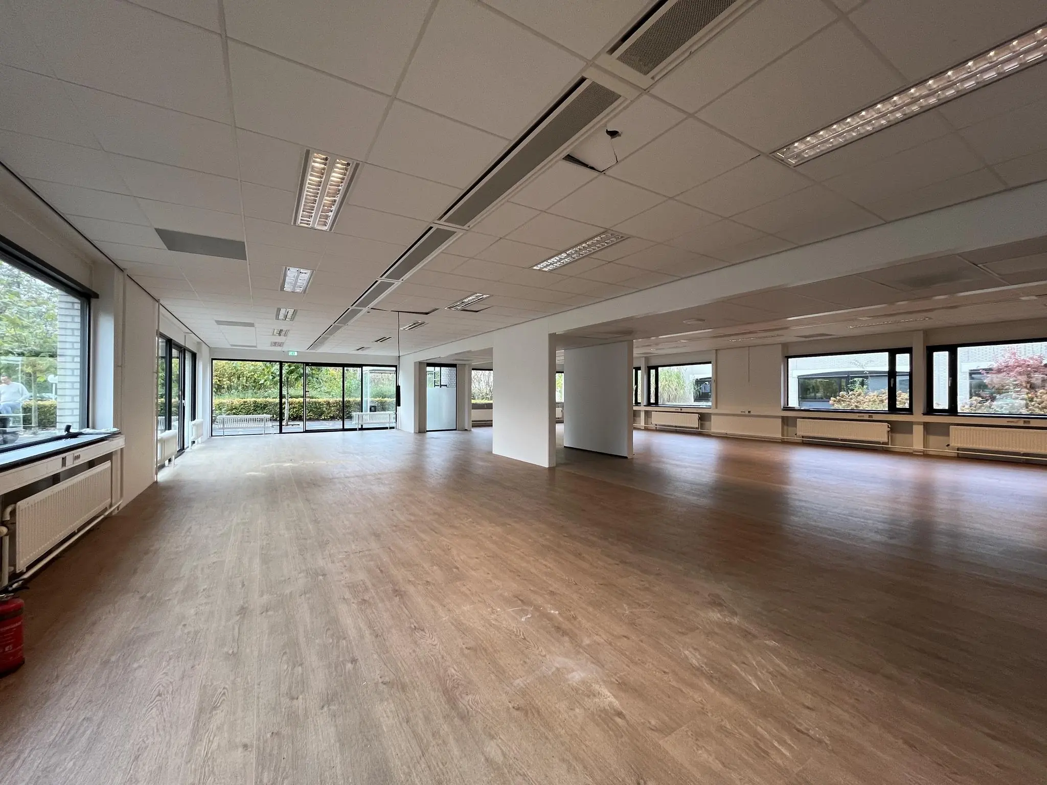 Ruime, lege kantoorruimte met houten vloer, systeemplafond en grote ramen aan de Burgemeester Verderlaan.